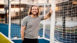 Jamie Farmer, smiling and leaning with his right arm against a soccer goalpost.